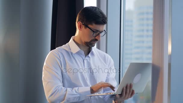 Un uomo d'affari concentrato tira su un computer portatile e guarda fuori da una finestra . — Video Stock