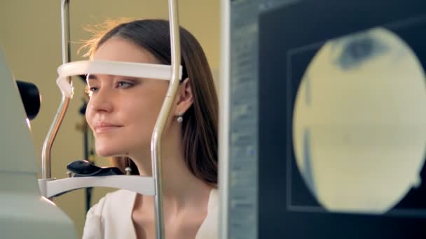 Een vrouw plaatst haar hoofd op een kin rest van een retinale camera. — Stockvideo