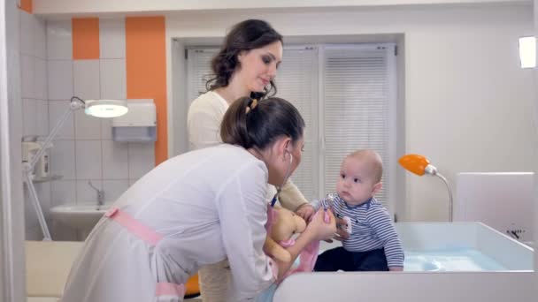 医師がクリニックの治療テーブルの上赤ちゃんと遊ぶ. — ストック動画