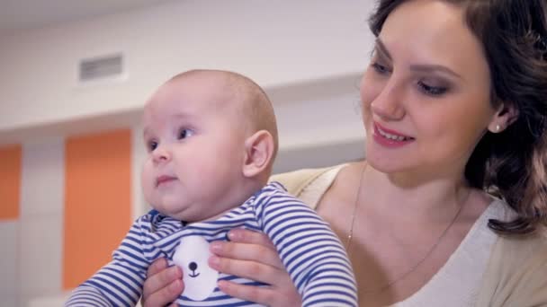 Aranyos baba mosolyogva ül az anyák karja. — Stock videók