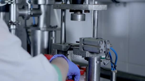 Um operador alimenta e remove garrafas de iogurte em uma máquina de vedação de pressão. 4K . — Vídeo de Stock