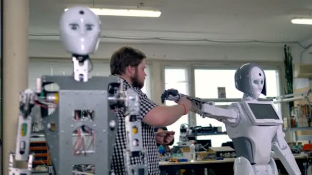 Een drukke ingenieur assembleert een van twee robots. — Stockvideo