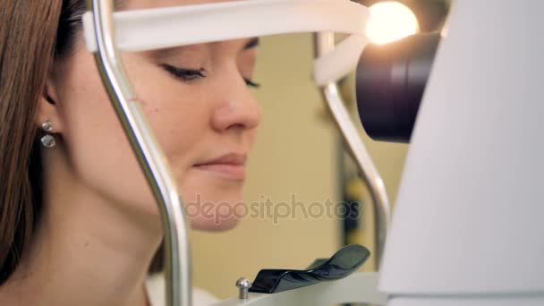 En kvinna lutar sig framåt för att ha ögonen testas av en medicinsk maskin. — Stockvideo