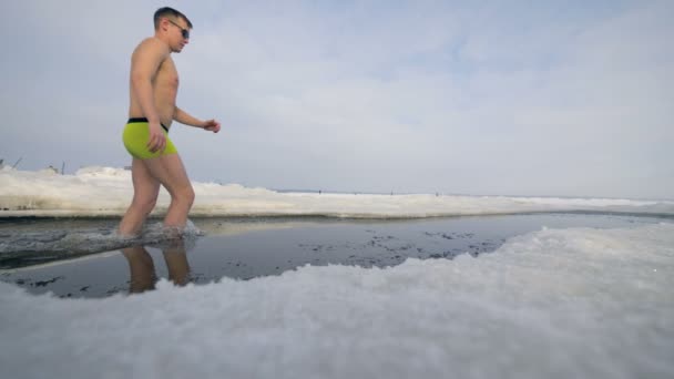 Un uomo entra in un buco di ghiaccio poco profondo nel fiume invernale . — Video Stock