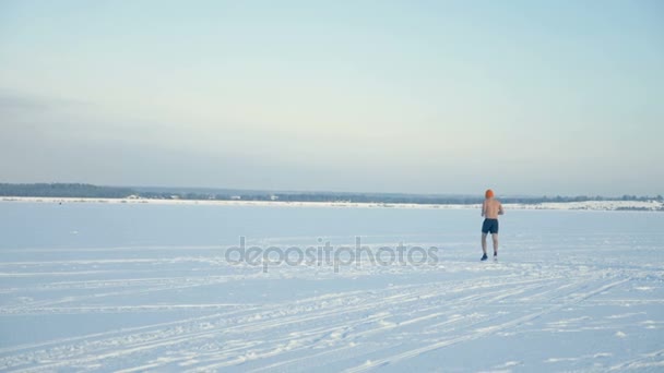 Ein Mann in sportlichen Shorts joggt auf einem weiten, schneebedeckten Feld. — Stockvideo