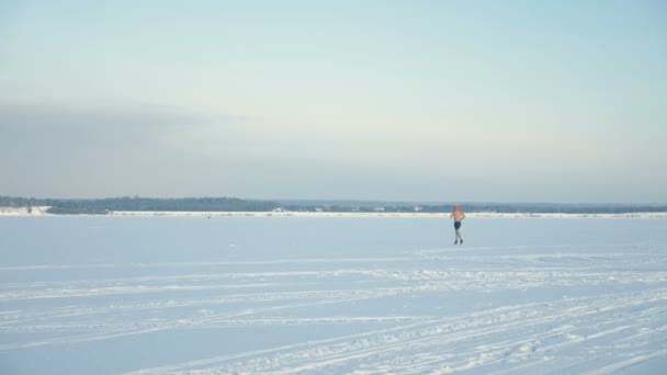 Silueta rozhalenou muž běží v dálce na zamrzlou řeku. 4k. — Stock video