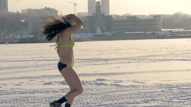 Жінка знімає капелюх під час бігу в купальнику взимку . — стокове відео