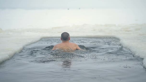 Mann schwimmt bei Schneefall in einem zugefrorenen Fluss. — Stockvideo