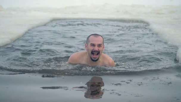 Egy férfi a jég lyuk úszik, és áll, hogy kap kívülről. — Stock videók