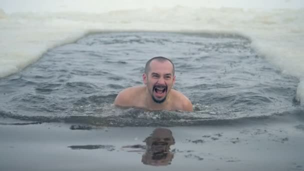 Un uomo nuota in un buco di ghiaccio e si alza per uscire . — Video Stock