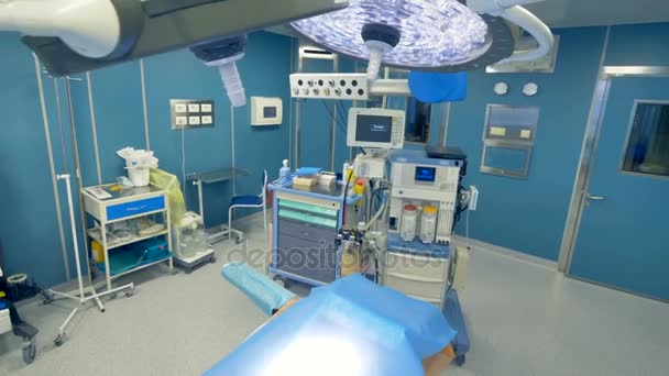 Una mesa quirúrgica vacía y sin usar bajo luces médicas cerca del equipo de trabajo. 4K . — Vídeos de Stock