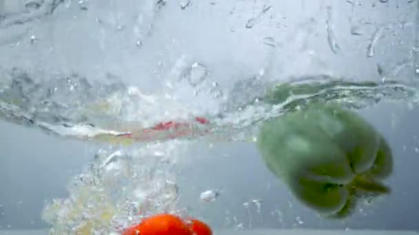 Three sweet peppers dive into clear water. — Stock Video