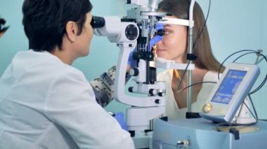 Doktor genç kadının gözleri incelenmesi ve microscoping makineye izlerken
