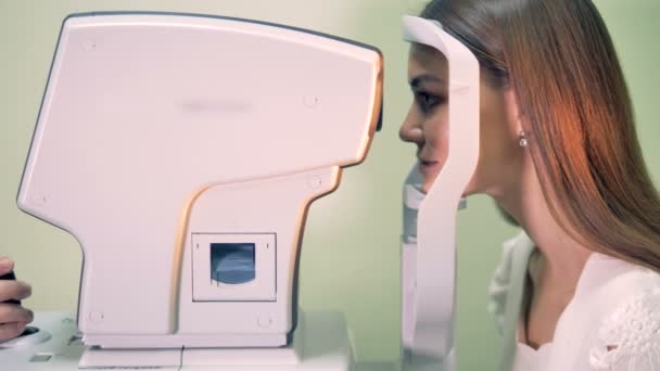 Side-on view of a young lady putting her head on a medical machine and getting her eyes checked — Stock Video