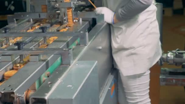 Las galletas terminadas se mueven a lo largo de la cinta transportadora mientras el trabajador de la fábrica controla el proceso — Vídeos de Stock