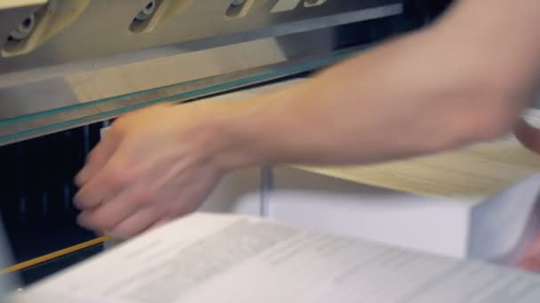 Працівник обертається навколо паперу, чиї непарні ребра відрізаються промисловим різаком . — стокове відео