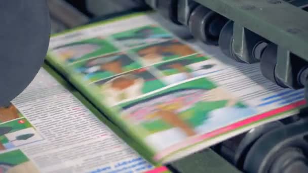 Close up van tijdschriften krijgen van een transportband onder een rollende press één voor één — Stockvideo