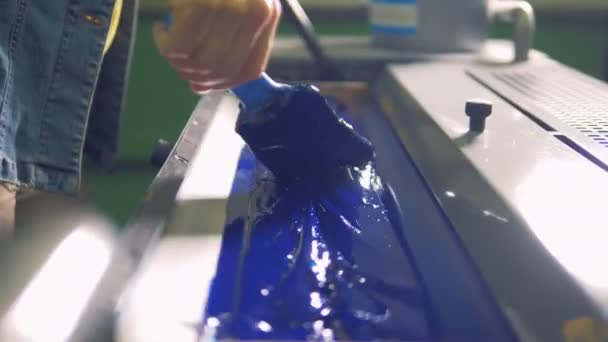 An employee is passing a brush over blue paint in a printing tray — Stock Video