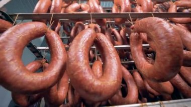 Tütsülenmiş sosis halkaları üzerinde metal duruyor, alt görünümü asılı olan.