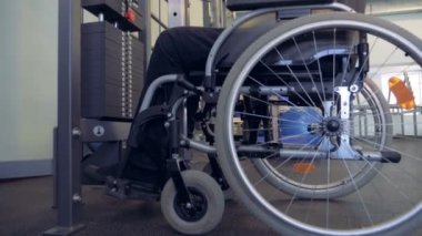Engelli biri tekerlekli sandalyede otururken bir spor salonunda ağırlık kaldırma yan görünüm
