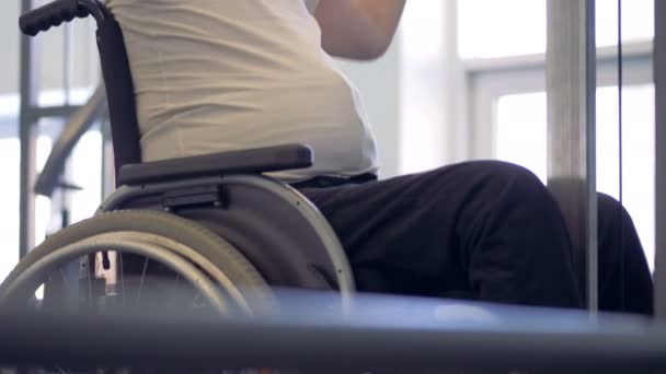 Un hombre discapacitado está sentado en una silla de ruedas y haciendo ejercicios con una barra de metal — Vídeos de Stock