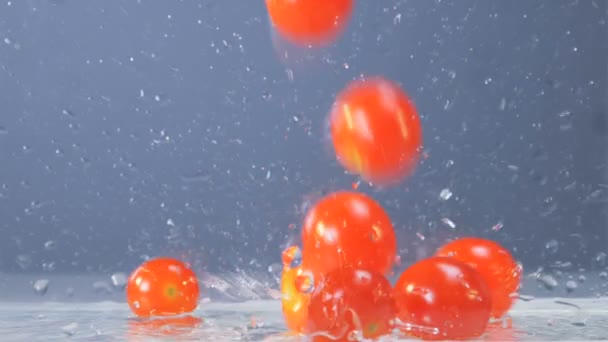 Los tomates están cayendo en un recipiente transparente con un poco de agua en la parte inferior — Vídeo de stock