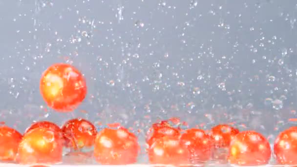 Orange tomatoes are rapidly falling into a tank with some water at the bottom — Stock Video