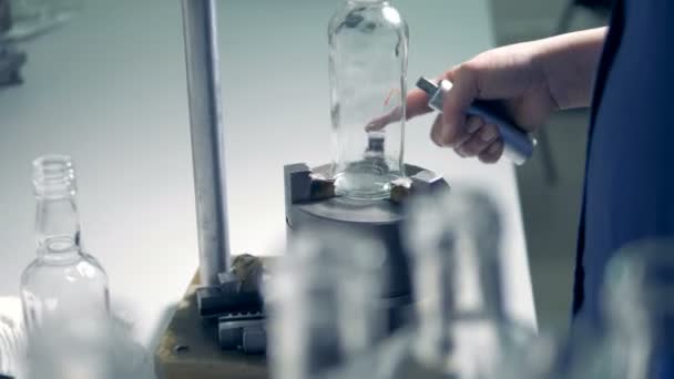 Factory employee is rotating a vitreous bottle placed on a metal stand — Stock Video