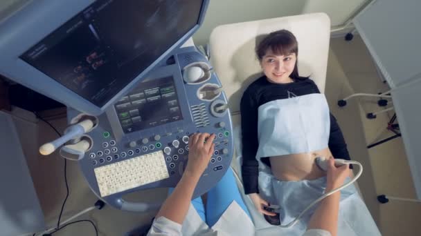 Mujer embarazada sonriente está observando su propio proceso de ultrasonido — Vídeos de Stock