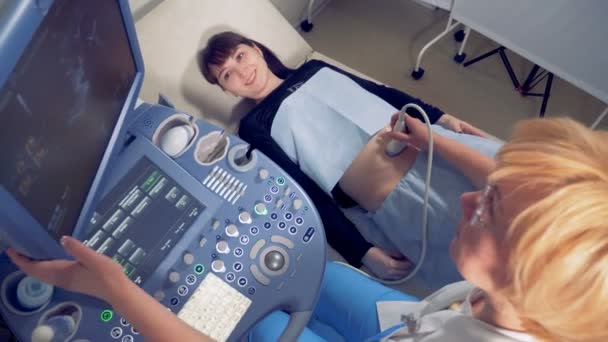 Feliz mujer embarazada sonriente mirando en la pantalla durante el procedimiento de ultrasonido . — Vídeos de Stock