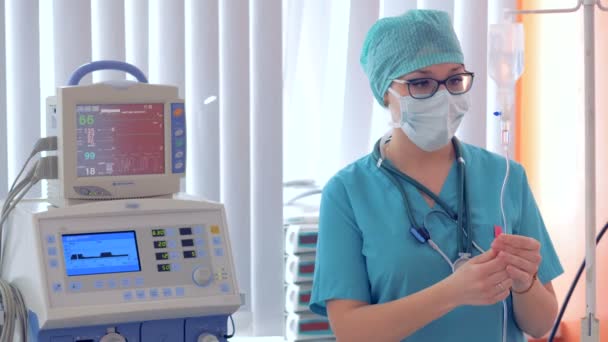 Une femme médecin câblage une fiole goutte à goutte et réglage des paramètres sur un moniteur — Video