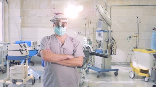 Retrato médico profesional. Médico masculino con un instrumento especial de chequeo en la cabeza está de pie en una sala de operaciones — Vídeos de Stock