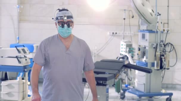 Cirujano profesional masculino camina y se detiene delante de una cámara mientras mira directamente en ella — Vídeo de stock
