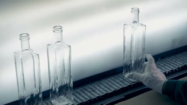 Un trabajador de la fábrica mira botellas de vidrio sobre un fondo claro, tratando de encontrar defectos. 4K . — Vídeo de stock