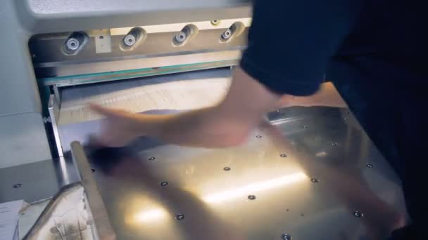 A man is putting a sheaf of paper under an industrial cutter and adjusting it — Stock Video
