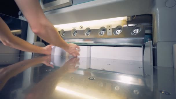 Un hombre está poniendo cuatro pilas de papel debajo de un cortador que corta sus lados — Vídeos de Stock