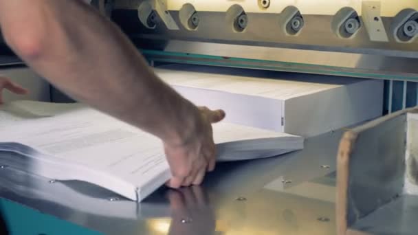 A stack of formsheets is being added to the other pile of paper and they are moved under a cutter by the man — Stock Video