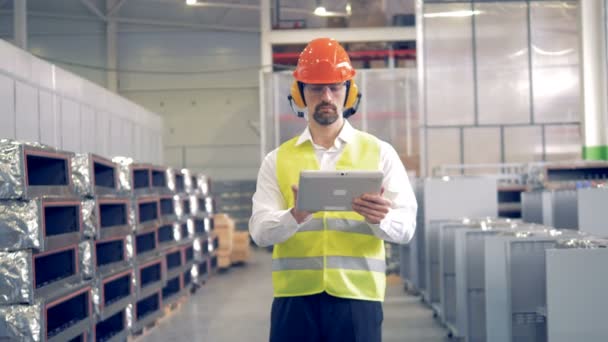 Um homem trabalha em instalações industriais, verificando informações em seu tablet . — Vídeo de Stock