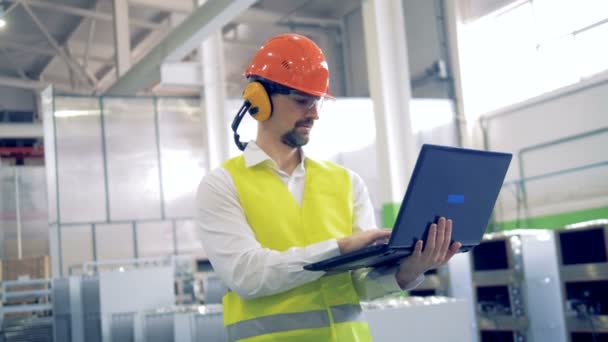 Człowiek w kask działa na laptopie w fabryce przemysłowej. — Wideo stockowe