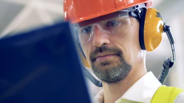 A man in hard hat works on his laptop at a warehouse, close up. — Stock Video