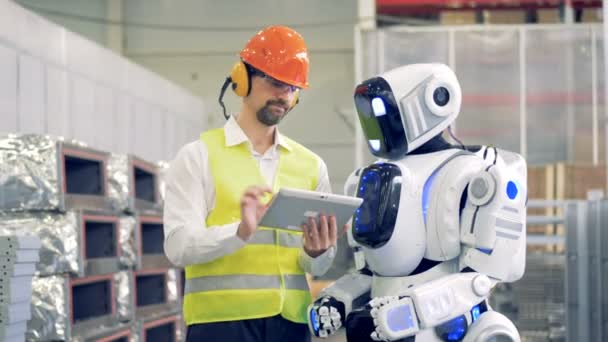 Travailleur masculin parle à un robot, lui montrant des informations sur une tablette, puis tape sur un moniteur de robots. 4K . — Video