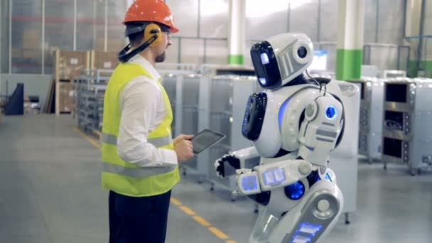 Un hombre habla con un robot en una fábrica — Vídeos de Stock