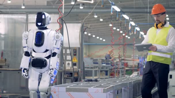 En arbetstagare styr en robot med en surfplatta på fabriksgolvet. — Stockvideo