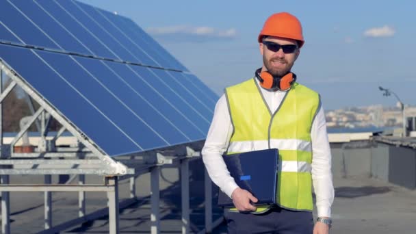 Um trabalhador sorri para a câmera, enquanto está perto de painéis solares e segurando um laptop. 4K . — Vídeo de Stock