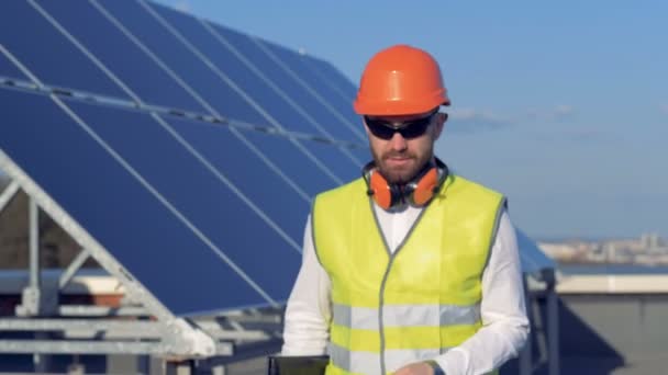 Un ingénieur se tourne vers la caméra et sourit, debout sur le toit avec un ordinateur portable. 4K . — Video