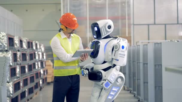 Hombre empleado de la fábrica está explicando algo a un robot y la regulación de sus ajustes — Vídeos de Stock