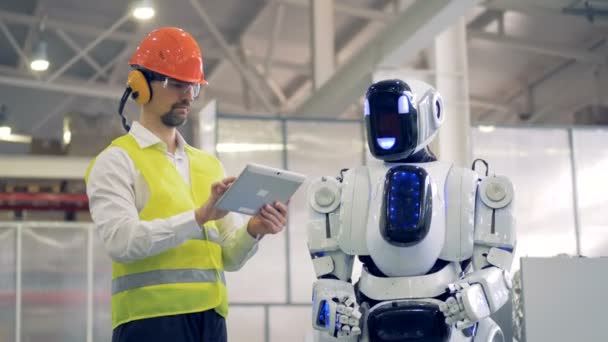 Menneskeaktige roboter kommer til en fabrikkarbeider som viser noen gester. – stockvideo