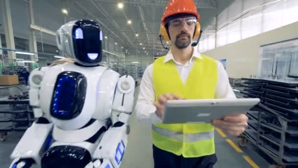 Trabajador de fábrica humano y un robot están caminando juntos en las instalaciones de la fábrica — Vídeos de Stock