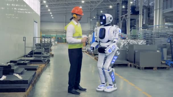 Trabalhador da fábrica masculino está controlando remotamente o robô e eles estão andando juntos — Vídeo de Stock