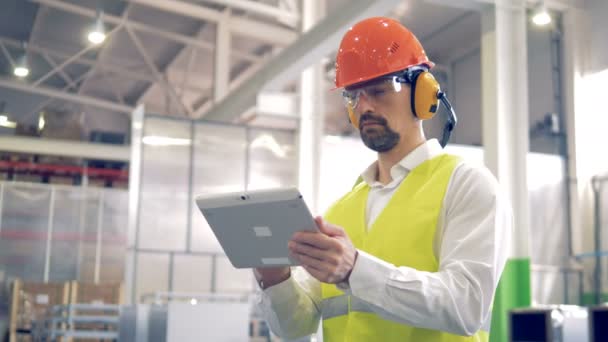 Fabrikarbeiter steht und arbeitet mit seinem Tablet in einem Fabriklager. — Stockvideo